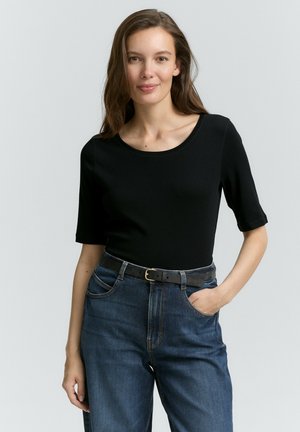 Haut noir à manches courtes en matière lisse, associé à un jean en denim bleu taille haute avec une ceinture noire et un design classique à cinq poches.