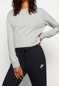 Felpa grigia con scollo a girocollo e logo Nike ricamato in bianco, abbinata a pantaloni jogger neri con cintura elastica e logo.