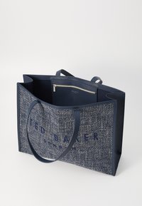 Marineblauwe draagtas van textuurstof met blauwe lederen rand. Bevat twee handvaten, een interne ritszak en een reliëf logo van het merk.