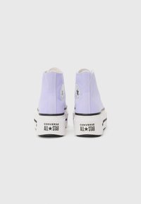 Baskets montantes en toile lilas avec semelles en caoutchouc blanches, arborant des rayures noires et des patchs de logo classiques.