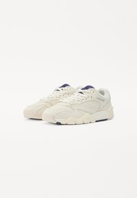 Lacoste Sneakers mit einem cremefarbenen Obermaterial, strukturierten Akzenten, durchbrochenen Details und einem blauen Akzent an der Sohle. Schnürdesign mit runder Zehenpartie.