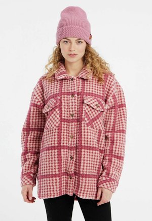 Roze en witte geruite fleece shirt met twee borstzakken en bruine knopen, gecombineerd met een lichtroze gebreide beanie muts.