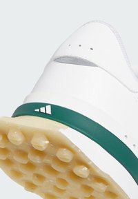 Chaussure en cuir blanc avec un talon arrondi, une semelle intermédiaire en caoutchouc vert et une semelle extérieure en caoutchouc texturé dotée de crampons hexagonaux antidérapants.