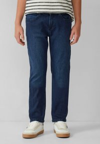 Jeans de mezclilla azul oscuro con corte recto, que cuentan con bolsillos delanteros, trabillas para el cinturón y una textura ligeramente desgastada. Llevados con zapatillas blancas.