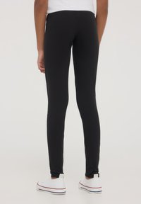 Czarne legginsy wykonane z elastycznej tkaniny, dopasowany krój, długość do kostek. W połączeniu z białymi trampkami z niebieskimi akcentami.