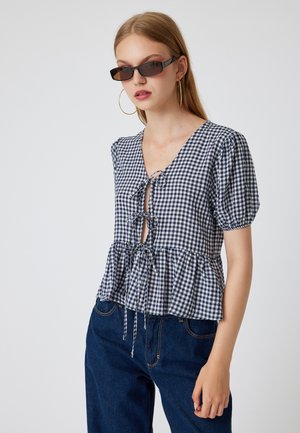 Blauw en wit geruite blouse met pofmouwen, V-hals, strikdetails bij de borst en taille, peplumzoom, gedragen met donkerblauwe spijkerbroek.