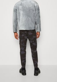 Szara, teksturowana, oversize'owa kurtka z długimi rękawami; w zestawie z czarnymi spodniami cargo w kamuflażu z bocznymi kieszeniami. Całość uzupełniają czarne sneakersy.