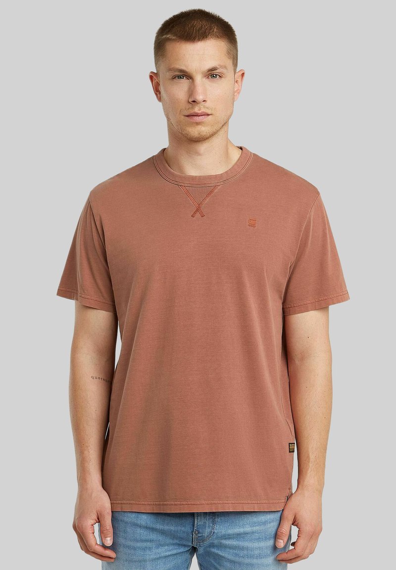 T-shirt a maniche corte color ruggine realizzato in cotone, con scollatura a girocollo, delicata cucitura a croce e un piccolo logo del marchio sul petto.