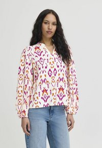 Long-sleeve blouse in white fabric with vibrant pink, orange, and purple ikat pattern, featuring a v-neck and gathered sleeves.