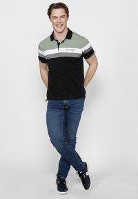 Polo tričko v zelených, bielych, sivých a čiernych pruhoch, s golierom a logom, spárované s modrými džínami a námorníckymi teniskami.