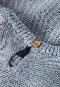 Vaaleansininen neulottu neulekuvio, jossa on resorikaulus ja yksittäinen koristeellinen puunappi.