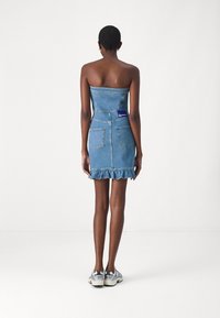 Jeans obleka s prilegajočim topom brez naramnic, drsajočim robom in dvema zadnjima žepoma. Svetlo modra barva z teksturiranim finišem in oznako na hrbtu.