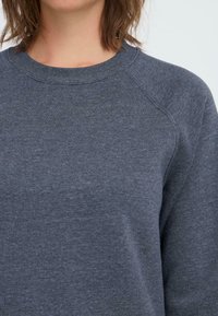 Sweatshirt gris foncé avec un col rond, des manches raglan et un tissu doux et texturé. Design simple sans motifs ni accents visibles.
