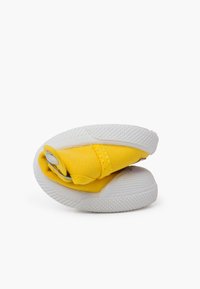 Žlutá plátěná bota s bílou gumovou podrážkou, zakřivený design, texturovaná tkanina a skládací funkce pro kompaktní uložení.