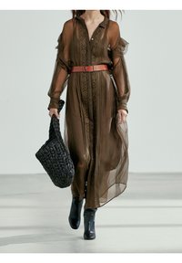 Tunn brun lång klänning med texturerad tyg, knappstängning fram och intrikata mönster. Kombinerad med ett rött bälte och en svart vävd handväska.