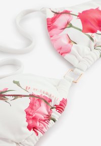 Haut de bikini blanc avec imprimé floral rose, bords froncés, bretelle ajustable et détail anneau en métal.