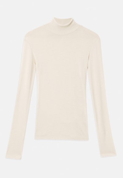 Haut à col roulé crème à manches longues en tissu doux et léger. Doté d'un design ajusté avec des coutures lisses et un col étroit.