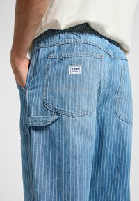 Pantaloni in denim blu chiaro a righe con tasca applicata e logo Lee Workwear. Presentano cuciture in vista e un design dalla vestibilità rilassata.