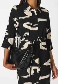 Abito nero con motivi astratti beige, design con bottoni e vita regolabile. Accompagnato da una borsa nera lucida.