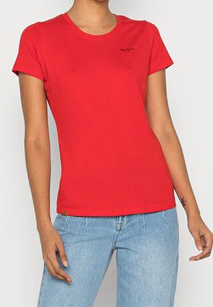 Kvinde iført en ensfarvet rød T-shirt med korte ærmer og lille sort tekst på venstre bryst, kombineret med lyseblå jeans.