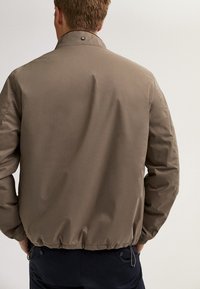 Brown, lightweight bomber jacket with a smooth texture, elastic hem, and collared neck. Features snap button detail. Back view displayed.