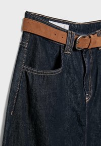 Temno modra jeans krila z sprednjim žepom in rjavim zamšastim pasom s srebrno zaponko na svetli podlagi.