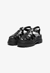 Black sandal shoes with a woven strap design, chunky platform sole, and adjustable ankle strap with metal buckle. Matte finish.