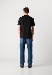 Zwarte t-shirt met korte mouwen en een ronde hals, gedragen met losse blauwe jeans. De denim heeft een lichte vervaging en beschikt over achterzakken.