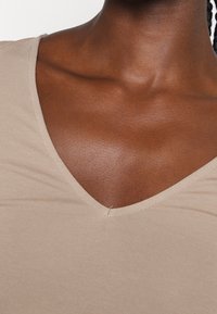 Top beige de canalé con escote en V, hecho de una tela suave, que presenta una forma ceñida y detalles de costura sutiles a lo largo del escote.