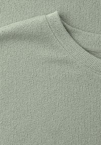 Gros plan sur un tissu tricoté vert clair avec un col côtelé, mettant en valeur la texture et le motif de points.