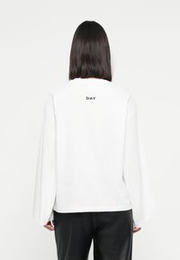 White long-sleeve sweatshirt with a relaxed fit, featuring the word "DAY" printed on the upper back in black. Paired with black pants.