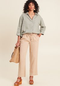 Lichtgroen linnen shirt met een kraag en knoopdetails, gecombineerd met beige linnen broek met trekkoord en bruine houten plateau-sandalen.