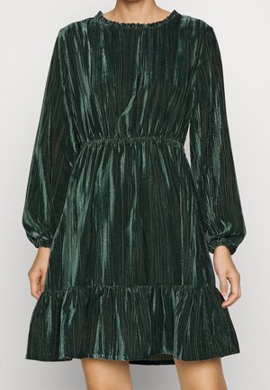 Green, velvet dress with a ribbed texture, long sleeves, a ruffled hem, and an elastic waist. Round neckline with a gathered edge.