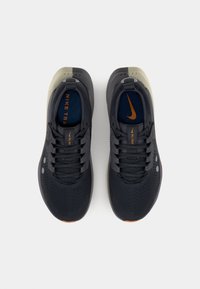 Nike running shoes with a black mesh upper, contrasting light grey accents, and a textured rubber sole. Additional details in orange.