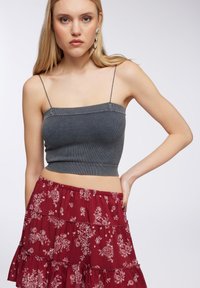 Top corto grigio a costine con spalline sottili abbinato a una gonna floreale rossa a strati con motivi bianchi e una vita elasticizzata.