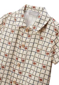Chemise à manches courtes en tissu beige présentant un motif en grille avec des accents colorés et des motifs d'ours, agrémentée de boutons en bois.