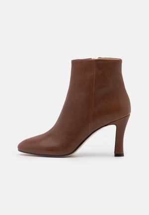 Bottine en cuir marron avec un bout pointu et un talon haut et fin. Texture lisse et design minimaliste qui renforcent son apparence élégante.
