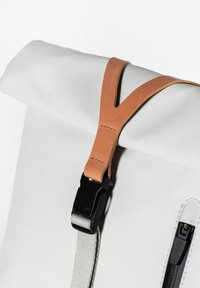 Weißer Rolltop-Rucksack mit braunem Ledergriff und schwarzem Schnallenverschluss, ausgestattet mit einem seitlichen Reißverschluss und strukturierter Oberfläche. Minimalistisches Design.