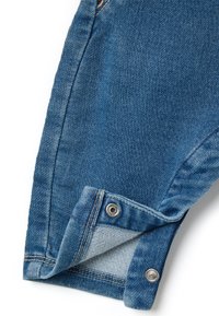 Blauwe denimstof met zichtbare stiksels, een plooi en een zilveren drukknoopsluiting bij de manchetten. Gestructureerd oppervlak met lichte vervaging en slijtage details.