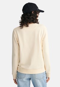 Creme sweatshirt med ribbet halsudskæring og manchetter. Kombineret med lyseblå denim, har den en afslappet pasform og en enkel, glat tekstur.