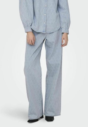 Lichtblauwe denimoutfit met een oversized gestreept shirt en wijde broek, aangevuld met een subtiele honingraat textuur en puntige zwarte schoenen.