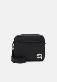 Borsa a tracolla sintetica nera con texture liscia, chiusura con zip e patch di un personaggio dei cartoni animati davanti. Include una tracolla regolabile.
