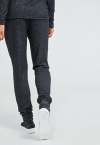 Black, sparkly joggers made of soft, stretchy material with a tapered leg design and gathered cuffs, paired with white sneakers.