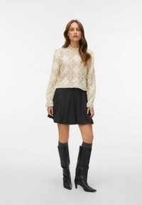 Biała koronkowa bluzka z diamentowymi wzorami, falbaniastym dekoltem i długimi rękawami; zestawiona z czarną rozkloszowaną spódnicą i czarnymi botkami do kolan.