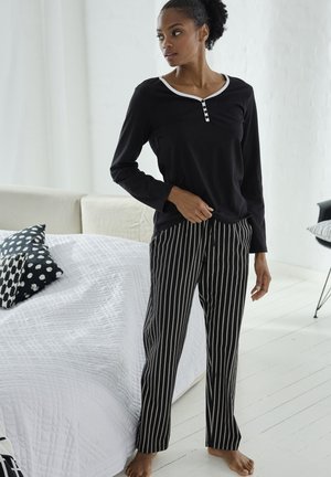 Schwarzes Langarmoberteil mit weißem Kragen und Knöpfen, kombiniert mit schwarz-weißen gestreiften Hosen. Glatter Stoff, tailliertes Design, entspannter Schnitt.