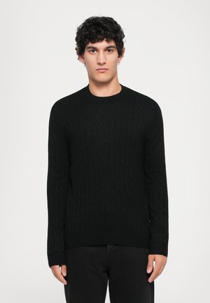 Black knit sweater featuring a diamond pattern, round neck, and ribbed cuffs, paired with dark jeans. Suitable for casual wear.