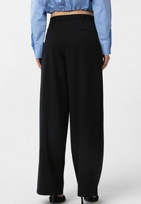 Wide-leg black trousers with a smooth texture and tailored fit. Features pockets at the back and a high waist design, paired with a blue blouse.