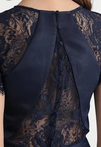 Middengrijs jurk met een kanten achterkant met bloemenpatronen, satijnen lijfje en zeven met stof bedekte knopen langs de achterste sluiting.