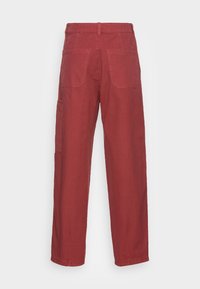 Pantalones de algodón rojos con un diseño de pierna recta, que cuentan con dos bolsillos traseros y un bolsillo lateral tipo cargo. La tela tiene una textura suave.