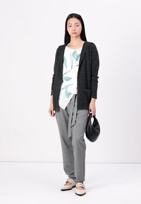 Gray cardigan over a white shirt with teal leaf pattern, paired with gray trousers and black bag. Smooth textures, relaxed fit design.
